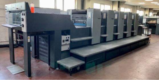 Na zdjęciu przedstawiona jest offsetowa 4‑kolorowa maszyna offsetowa z zespołem nakładającym lakier. Widoczna jest długa maszyna z panelem sterującym w przedniej części.