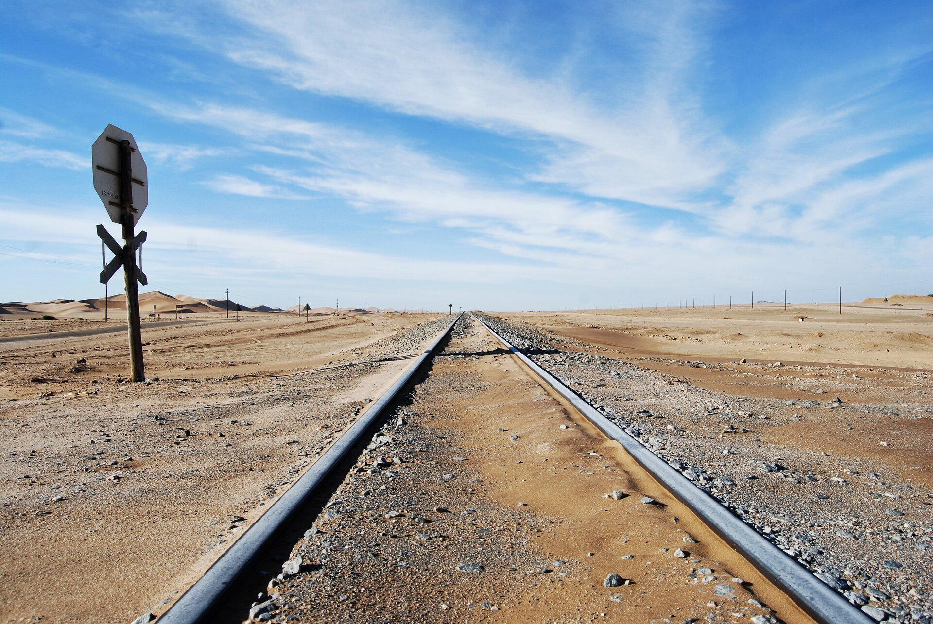 Zdjęcie przedstawiające tory kolejowe położone pośród jałowego, pustynnego terenu. Po lewej stornie znak stop.