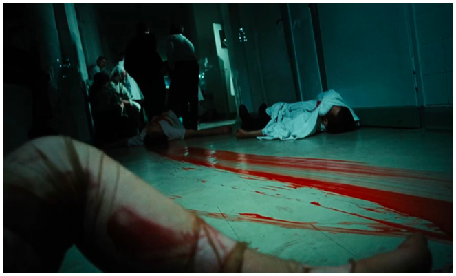 Fotografia przedstawia korytarz ukazany z perspektywy od dołu. Na pierwszym planie ukazana jest kobieca noga. Jest okryta cienkimi, porwanymi pończochami. W kilku miejscach jest zakrwawiona. Na podłodze, na drugim planie leżą ciała dwóch osób. Podłoga jest pobrudzona świeżą krwią. W głębi, po lewej stronie stoi grupa ludzi. Rozmawiają ze sobą.