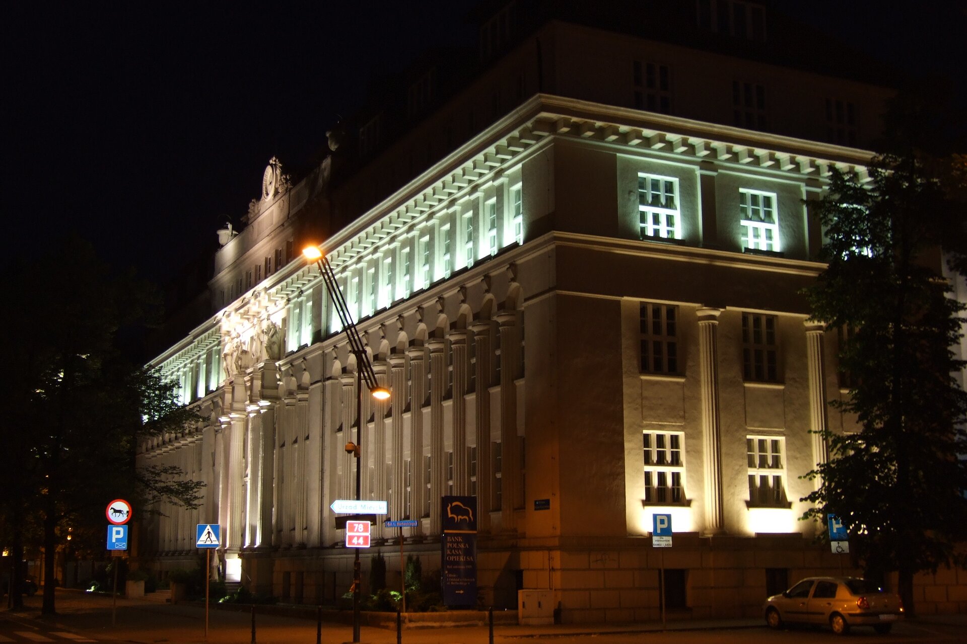 Kliknij żeby powiększyć Zdjęcie, które przedstawia Wojewódzki Sąd Administracyjny w Gliwicach. Zdjęcie przestawia podświetlony sąd porą wieczorową. Wejście zdobi portyk z dwukondygnacyjnymi kolumnami podtrzymującymi cokolik z rzeźbionymi postaciami robotników.