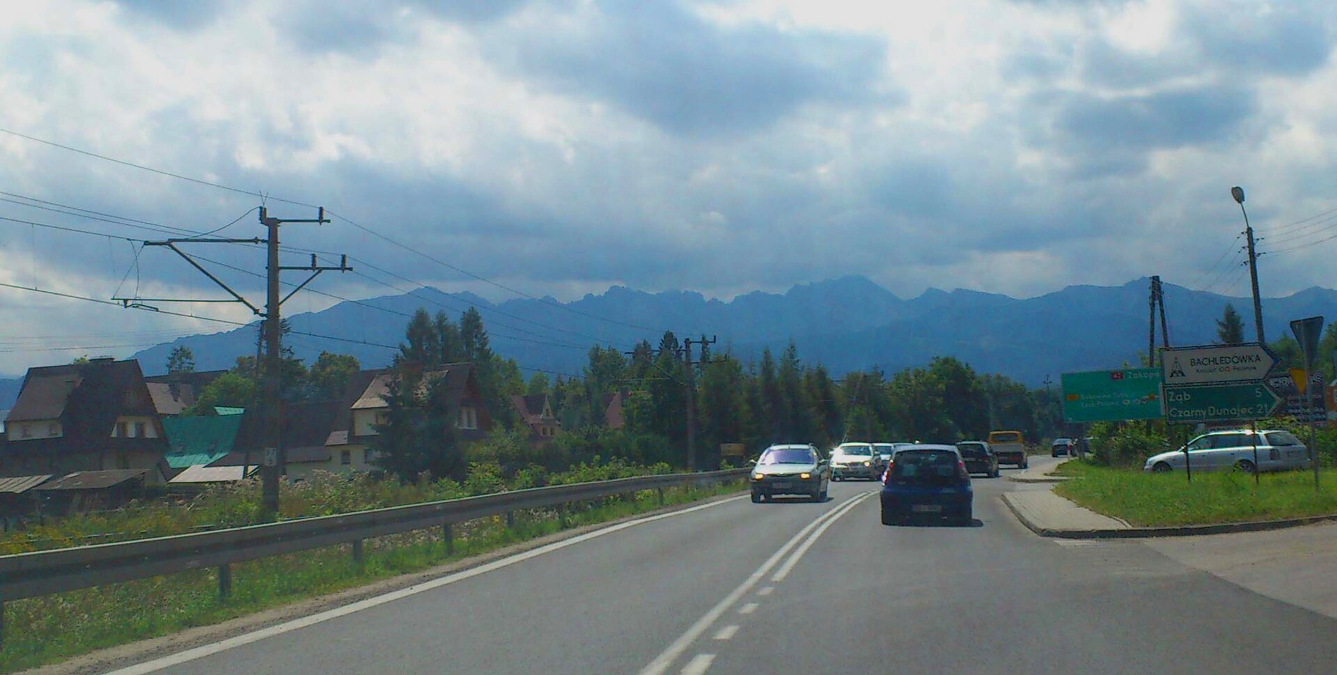Na zdjęciu droga asfaltowa, sznur samochodów, wzdłuż drogi linia kolejowa, w tle góry.