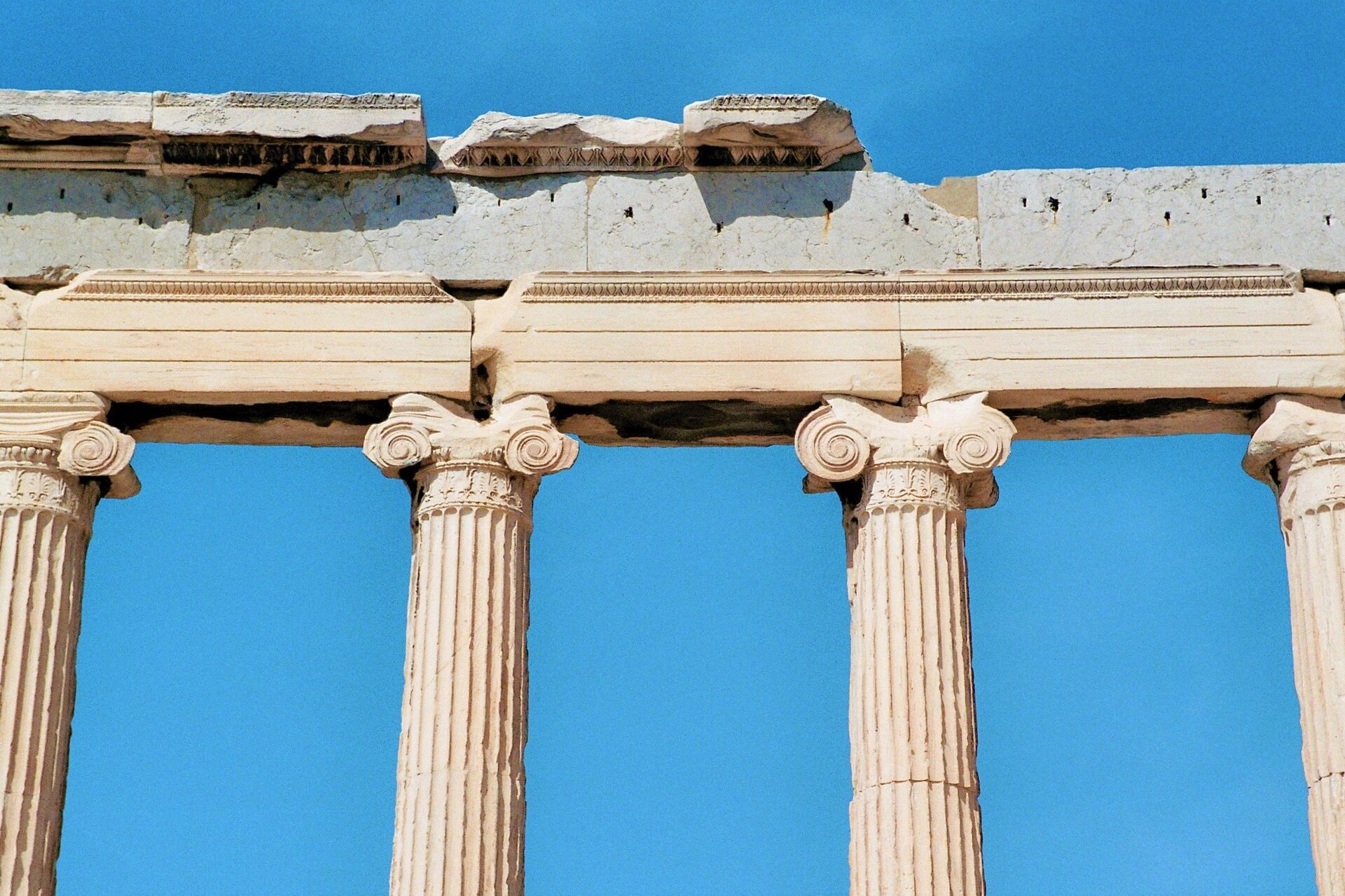 Zdjęcie przedstawia górny fragment zniszczonej świątyni. Ukazane są cztery kolumny i belkowanie. Kolumny mają głowice udekorowane ślimacznicami; trzony kolumn są żłobkowane. Tło stanowi bezchmurne niebo.