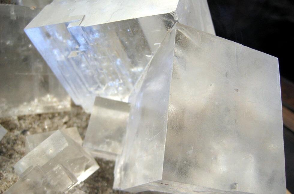 Zdjęcie prezentuje kryształ chlorku sodu czyli soli kamiennej. Można się w nim bez trudu dopatrzyć niemal idealnie prostopadłościennych struktur, a sam kryształ jest mlecznobiały i w dużym stopniu przezroczysty.