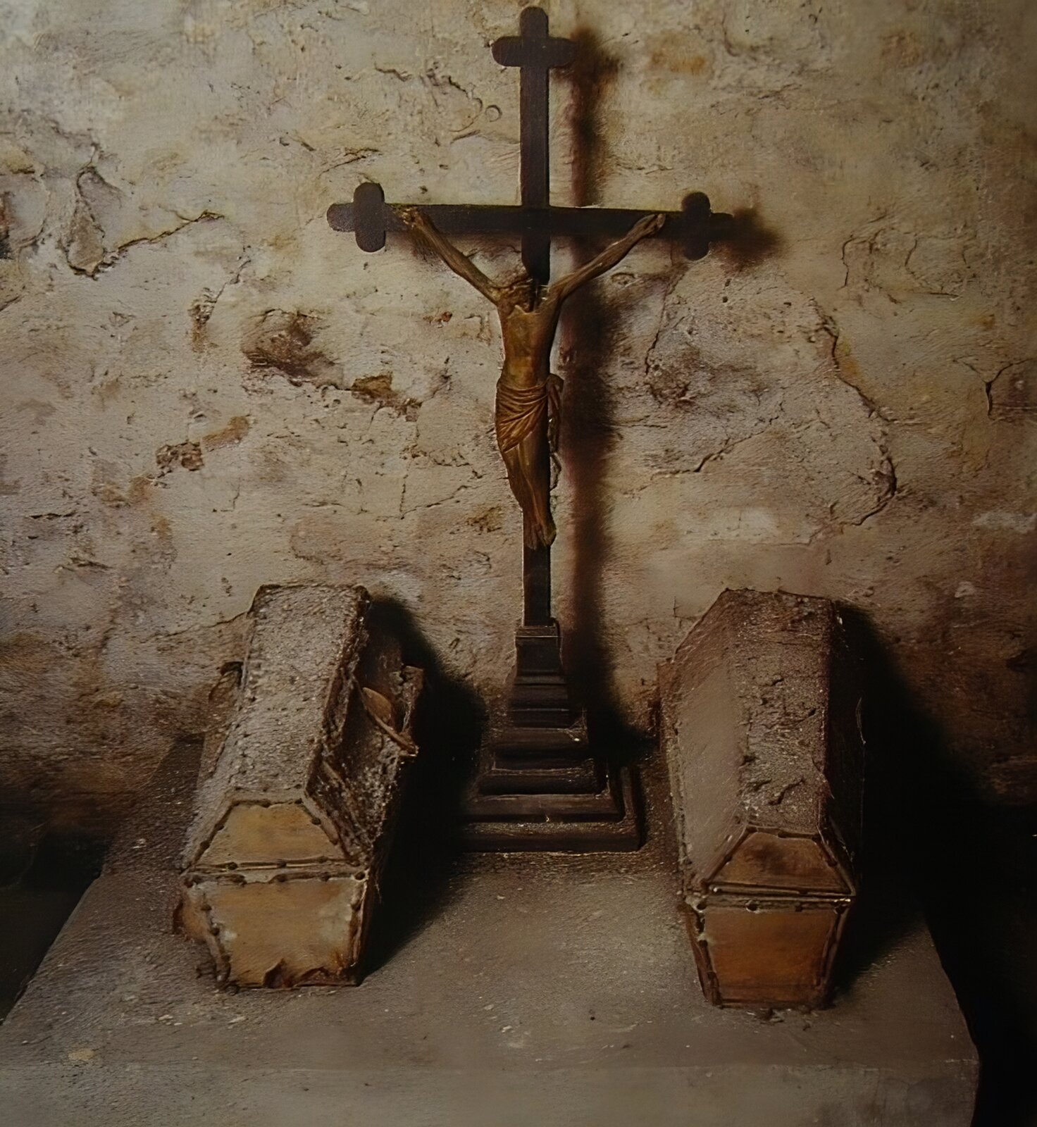 Zdjęcie współczesne z wnętrza krypty w kościele św. Anny. Na pierwszym planie widoczne dwie trumny o kształcie pięciobocznego graniastosłupa, leżące po obu stronach metalowego krucyfiksu z figurą ukrzyżowanego Chrystusa. W tle ściana krypty, mocno popękana i nosząca ślady zawilgocenia. 