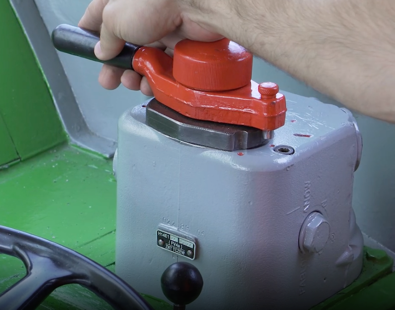 Zdjęcie przedstawia główny zawór maszynisty. Jest to czerwona dźwignia obracana w poziomie. Dłoń maszynisty trzyma dźwignię.