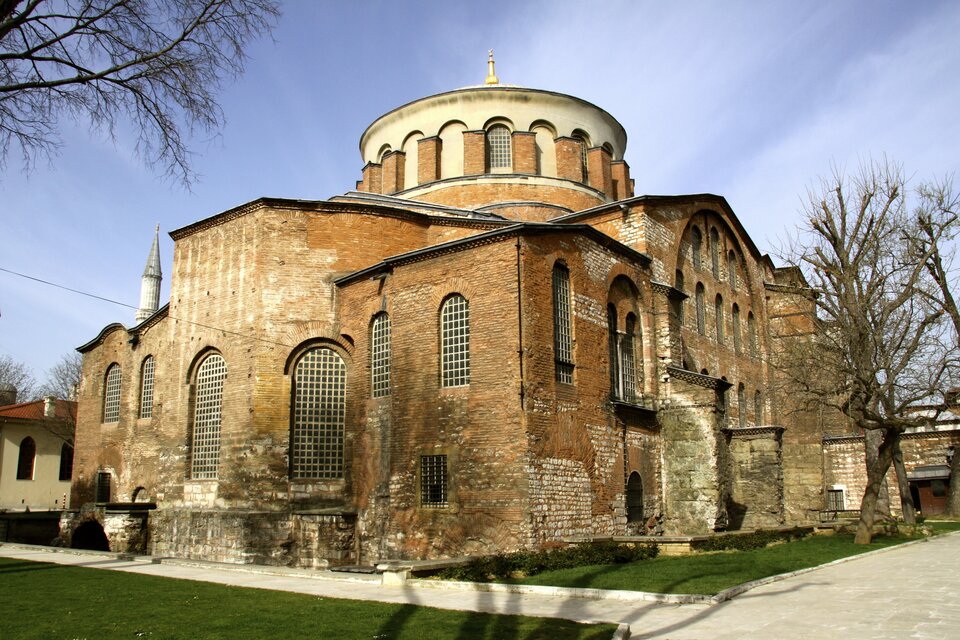 Zdjęcie współczesne Kościoła Hagia Eirene w Stambule. Bryła zewnętrzna jest zwarta, z prostymi murami z czerwonobrązowej cegły, z rytmicznie rozmieszczonymi oknami.