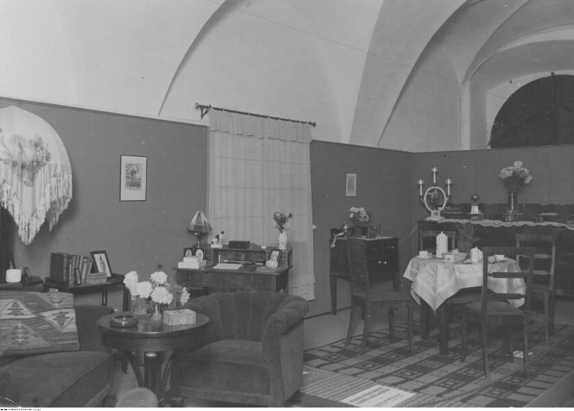 Zdjęcie przedstawia wnętrze dużej sali. Znajdują się w niej stoliki i krzesła, a także fotele.