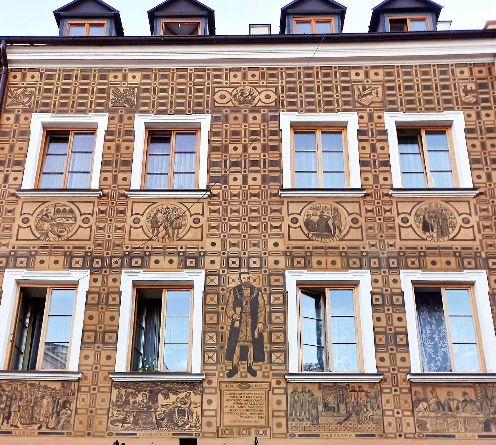 Zdjęcie przedstawia elewację (zewnętrzną ścianę) kamienicy starego miasta, ozdobionej ornamentem wyciętym w kolorowym tynku, tzw. sgraffito. Symetryczne ustawienie okien pozwala przeprowadzić oś symetrii między nimi. Jedna i druga strona tego podziału są podobne.