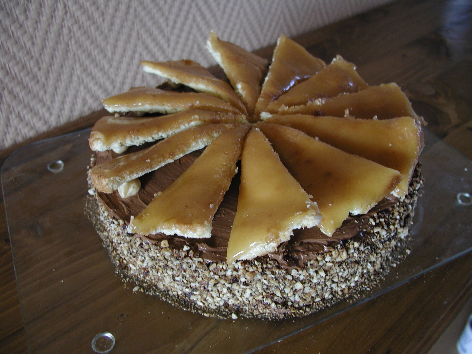 Zdjęcie okrągłego tortu czekoladowego, posypanego białymi wiórkami kokosowymi . Na wierzchu dekoracja z 12 kawałków ciasta biszkoptowego w karmelu. 