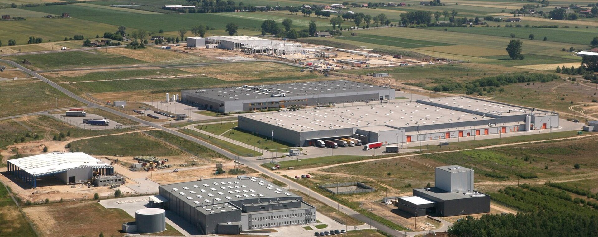 Na zdjęciu kompleks dużych hal magazynowych usytuowanych pod miastem. Dookoła pola.