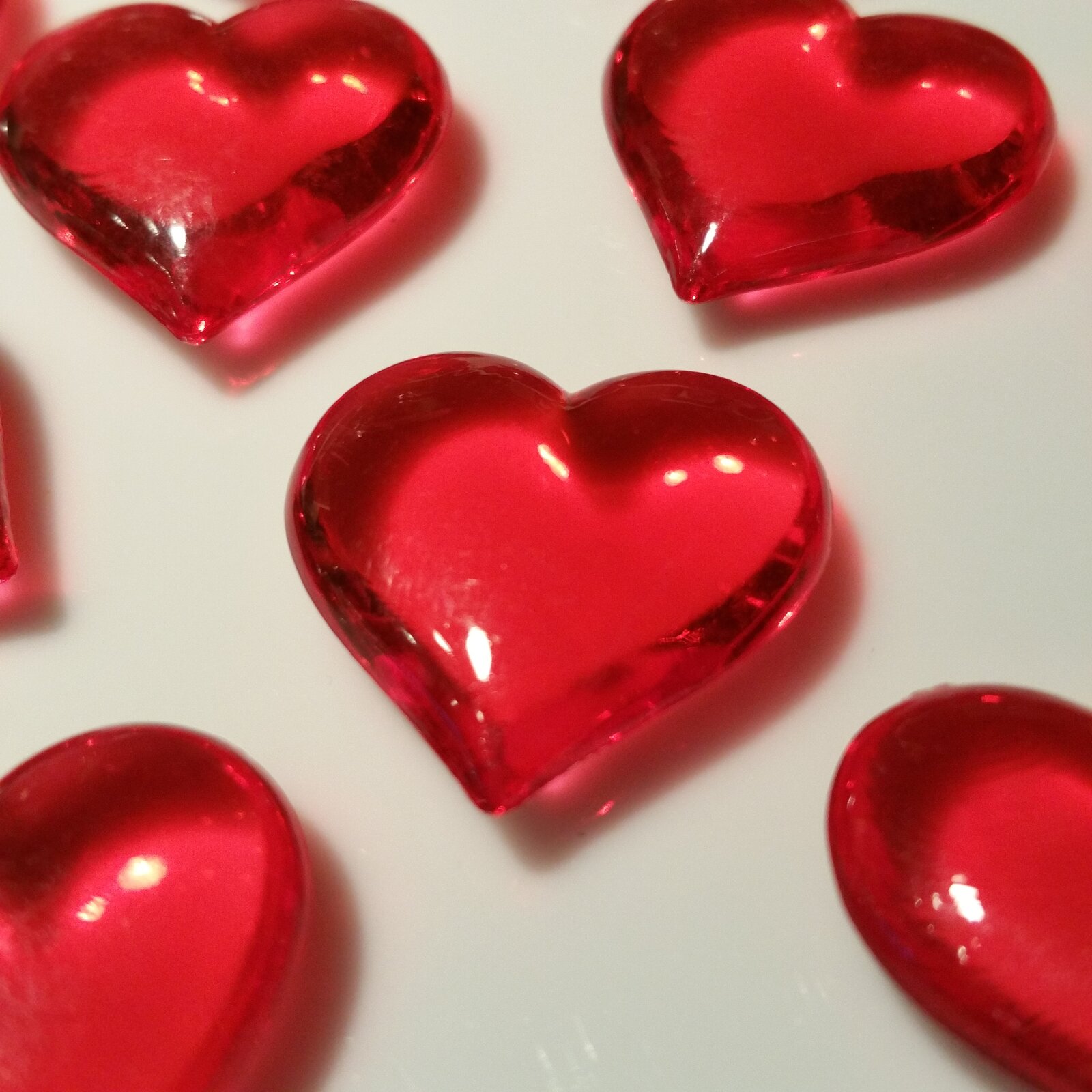 Grafika przedstawia czerwone, szklane serca, przezroczyste i błyszczące. Jest ich sześć, z czego pięć nie jest widoczne w całości.