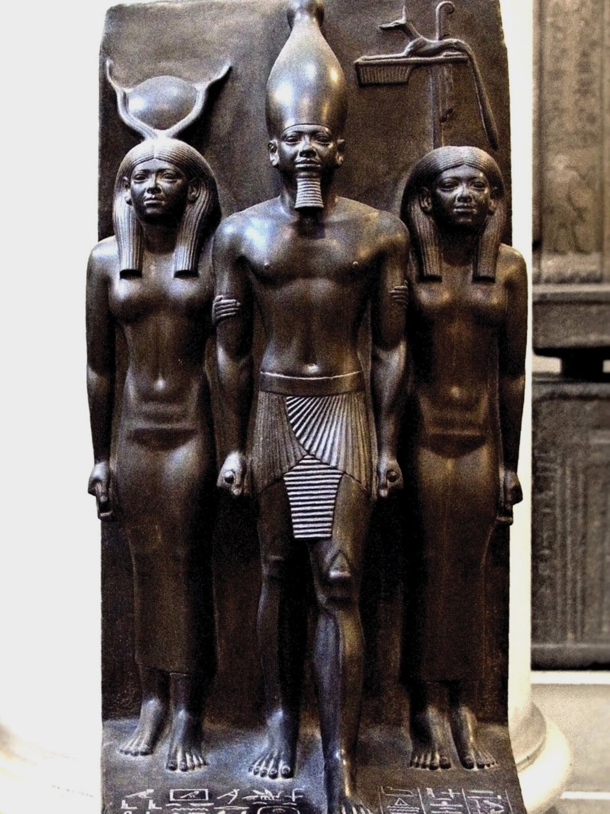 Zdjęcie przedstawia rzeźbę: trzy posągi pochodzące z czasów starożytnego Egiptu, tzw. Triada Mykerinosa. Mykerinos jest faraonem i kroczy pośrodku, po obu stronach postacie kobiet, boginii. Rzeźby wykonane są w kamieniu, mają gładką powierzchnię. Na podstawie tej rzeźby można zauważyć, na czym polega kanon przedstawiania postaci w starożytnym Egipcie, oparty na ścisłej hierarchizacji związanej z ustrojem politycznym. Faraon był przedstawiany jako największy, nieco z przodu, zawsze młody, o twarzy pozbawionej emocji, zawsze z przodu, z insygniami władzy.