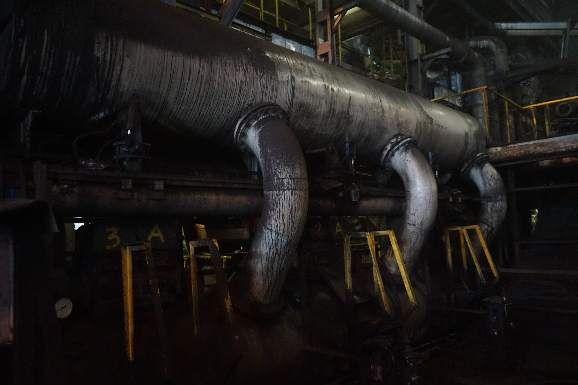 Na zdjęciu widoczna jest osadzarka widziana z boku. Osadzarka służy do wzbogacania głównie surowego węgla kamiennego oraz pozyskiwania żwiru i piasku przy równoczesnym wydzielaniu zanieczyszczeń organicznych i mineralnych. Centralnym elementem osadzarki jest podłużny cylindryczny zbiornik. Zbiornik jest o kształcie stalowej rury o dużej średnicy. Z boku  zbiornika odchodzą trzy rury. Tuty są połączone ze zbiornikiem połączeniem kołnierzowym. Na dole rur znajdują się półokrągłe zbiorniki. Pomiędzy nimi znajdują się żółte stalowe pręty. Pręty są o kształcie trapezu. Nad podłużnym zbiornikiem widoczna jest galera. Galera jest zabezpieczona żółtą balustradą.Osadzarka znajduje się w dużej hali przemysłowej.