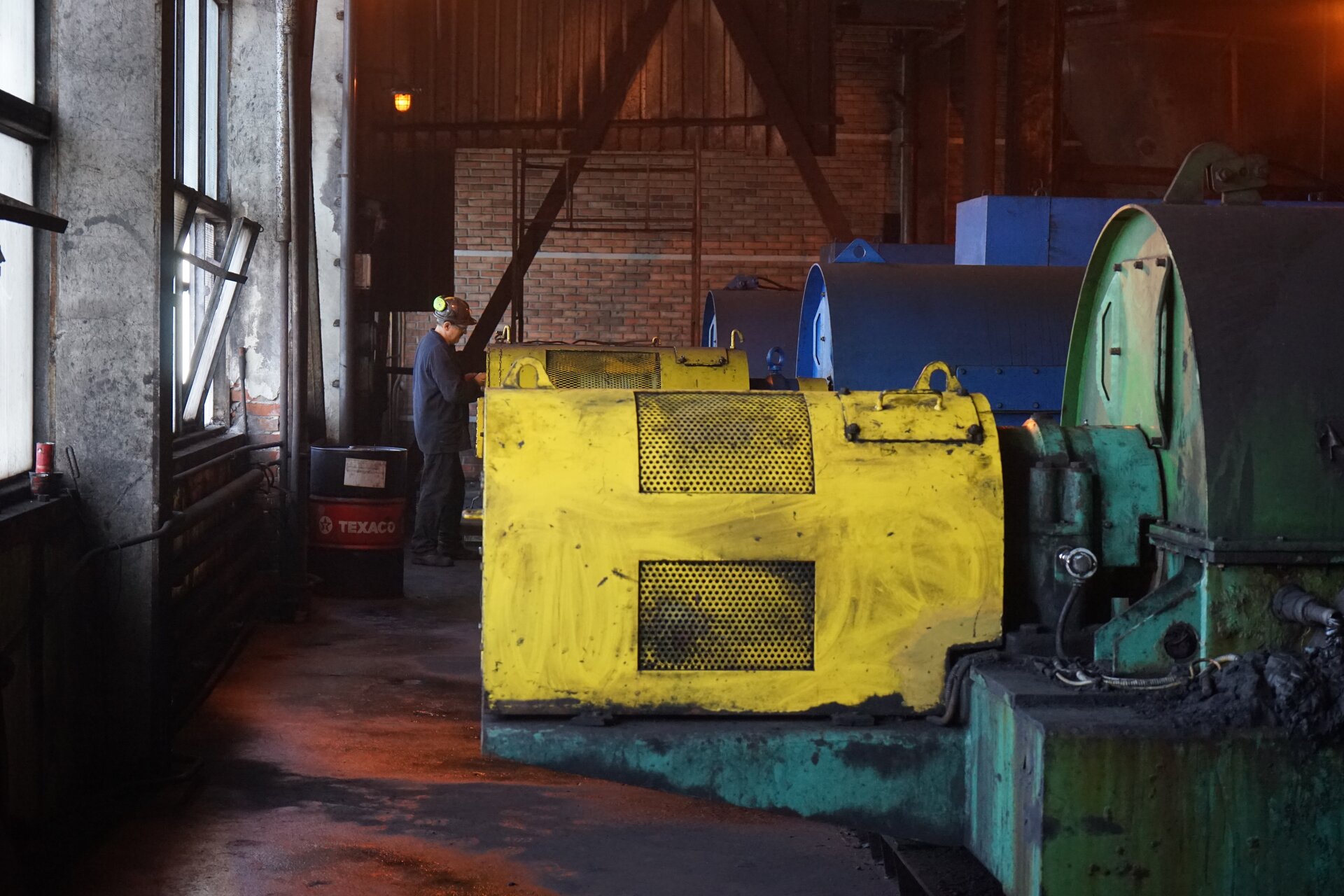 Zdjęcie przedstawia wirówkę sedymentacyjną. Urządzenie pozwala na odwodnienie dostarczonego koncentratu. Jest ono umieszczone w żółtej obudowie zaokrąglonej w górnej części. Z lewej strony w hali zakładu znajdują się okna. Poniżej zdjęcia znajduje się przycisk multimedialny z nagraniem audio. Treść nagrania jest zgodna z tytułem zdjęcia.