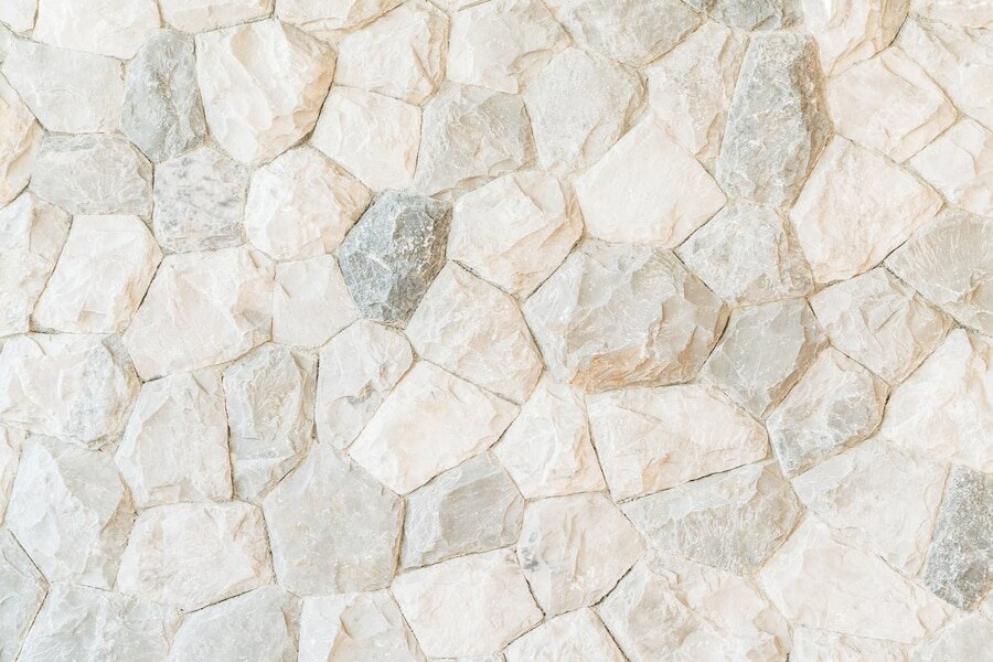 Zdjęcie przedstawia fragment ściany złożonej z jasnych kamieni o nieregularnym kształcie i fakturze groszkowanej.