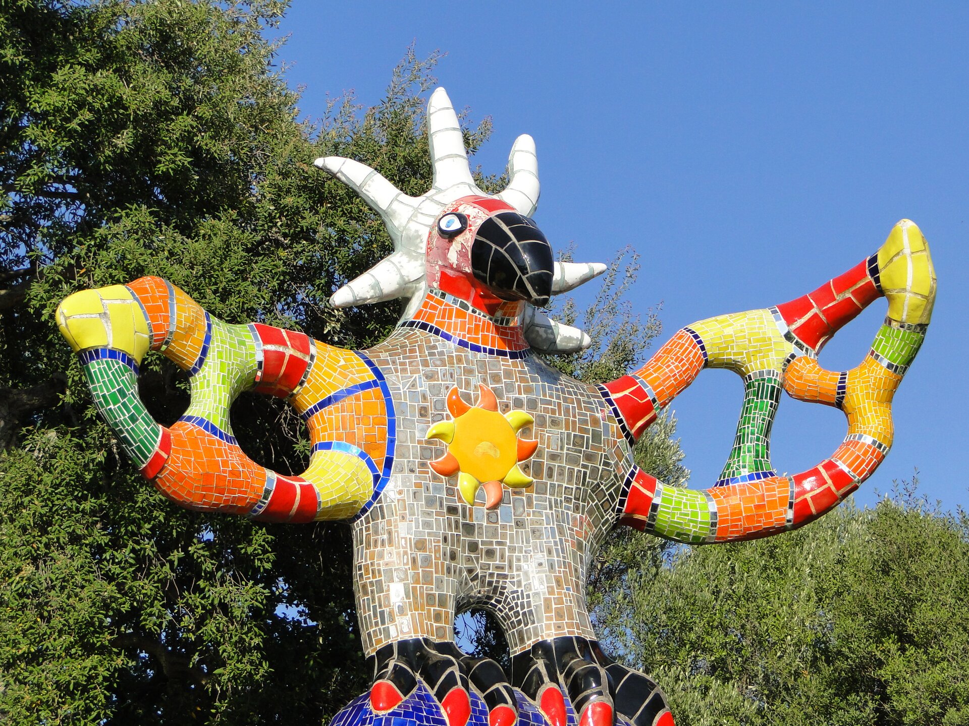 Ilustracja przedstawia pracę Niki de Saint Phalle „Ogród Tarota”. Znajduje się na w Toskanii we Włoszech. Fotografia została wykonana w 2011 roku. Przedstawiona została figura znajdująca się w ogrodzie. Wygląda na to, że jest to kolorowy ptak z długim i ostrym dziobem. W tle są liczne drzewa. Autorką pracy jest francuska rzeźbiarka oraz malarka. W swoich pracach bardzo często wykorzystywała motyw kobiecego ciała.