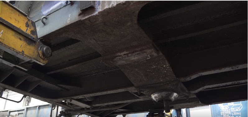 Zdjęcie przedstawia ostoję wagonu. Na zdjęciu widać ostoję wagonu. Jest to stalowa rama, na której oparte jest pudło wagonu. Zdjęcie zrobione jest z perspektywy od dołu.