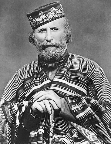 Na czarno‑białym zdjęciu znajduje się Giuseppe Garibaldi. Jest on ubrany w szeroki płaszcz ozdobiony w liczne poziome pasy. W rękach trzyma laskę. Na głowie ma ciemną czapkę we wzory. Ma siwą brodę. 