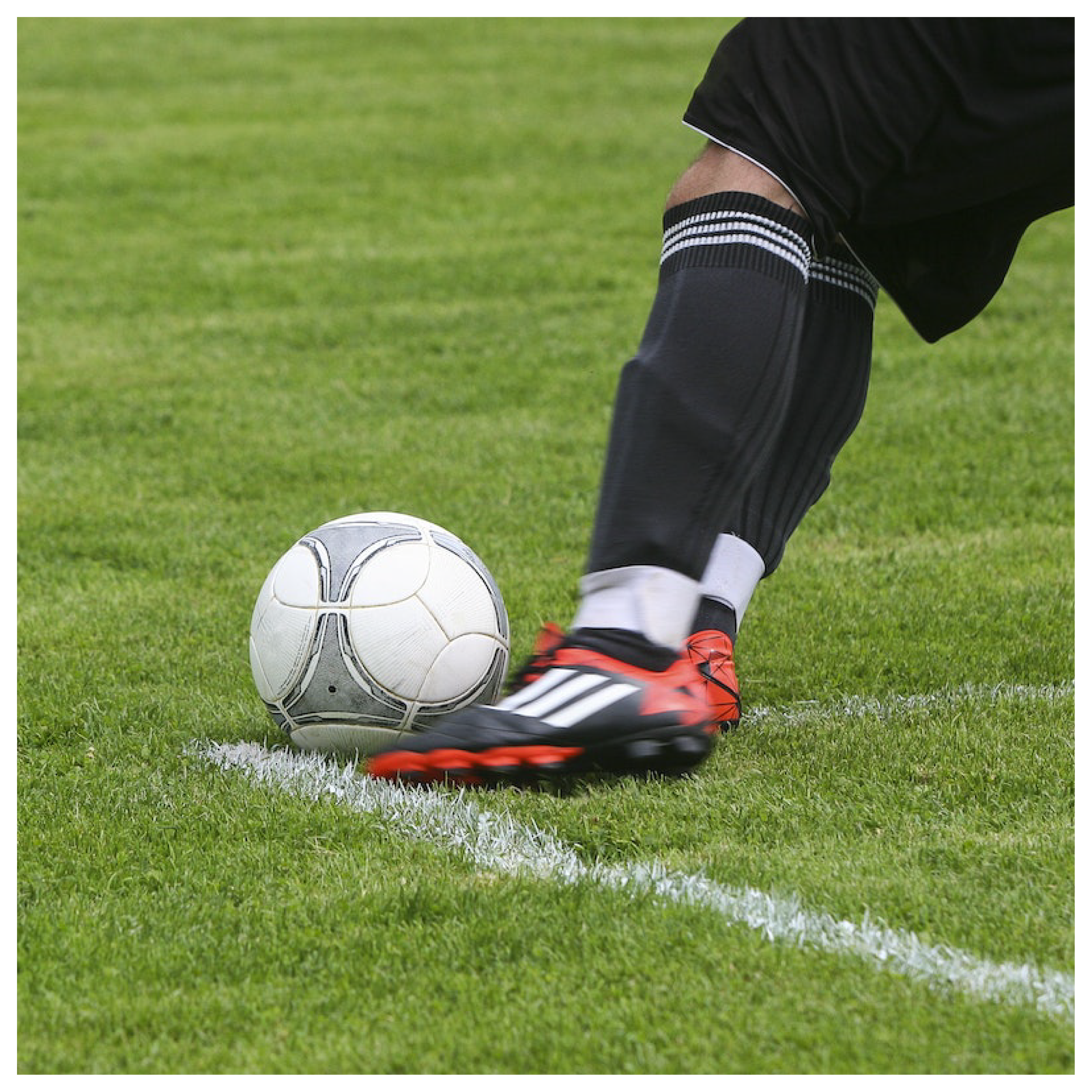 Obrazek przedstawia piłkę prowadzoną przez nogi piłkarza przy narożniku boiska.