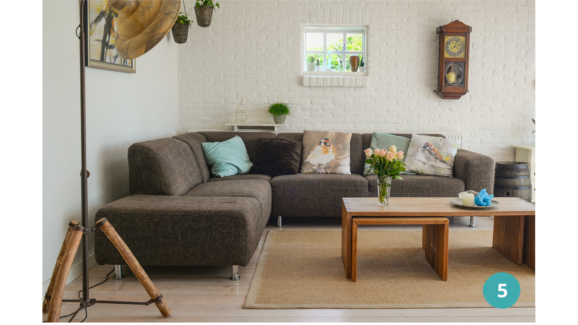 Zdjęcie przedstawia salon. W salonie stoi duża kanapa, przed nią stolik. Nad kanapą widoczne są: okno i wiszący zegar.