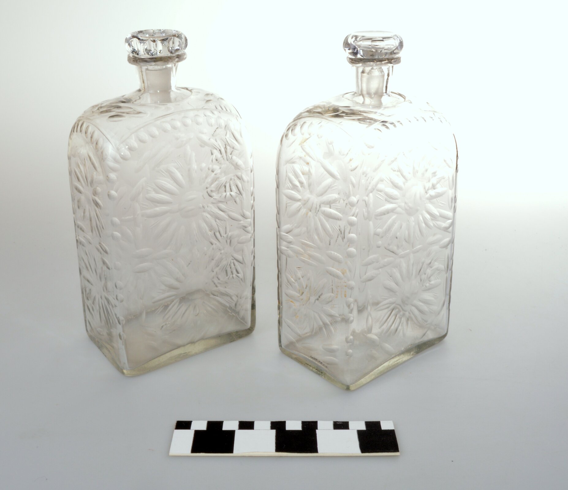 Ilustracja przedstawia dwie szklane butelki zdobione kwiecistym wzorem.