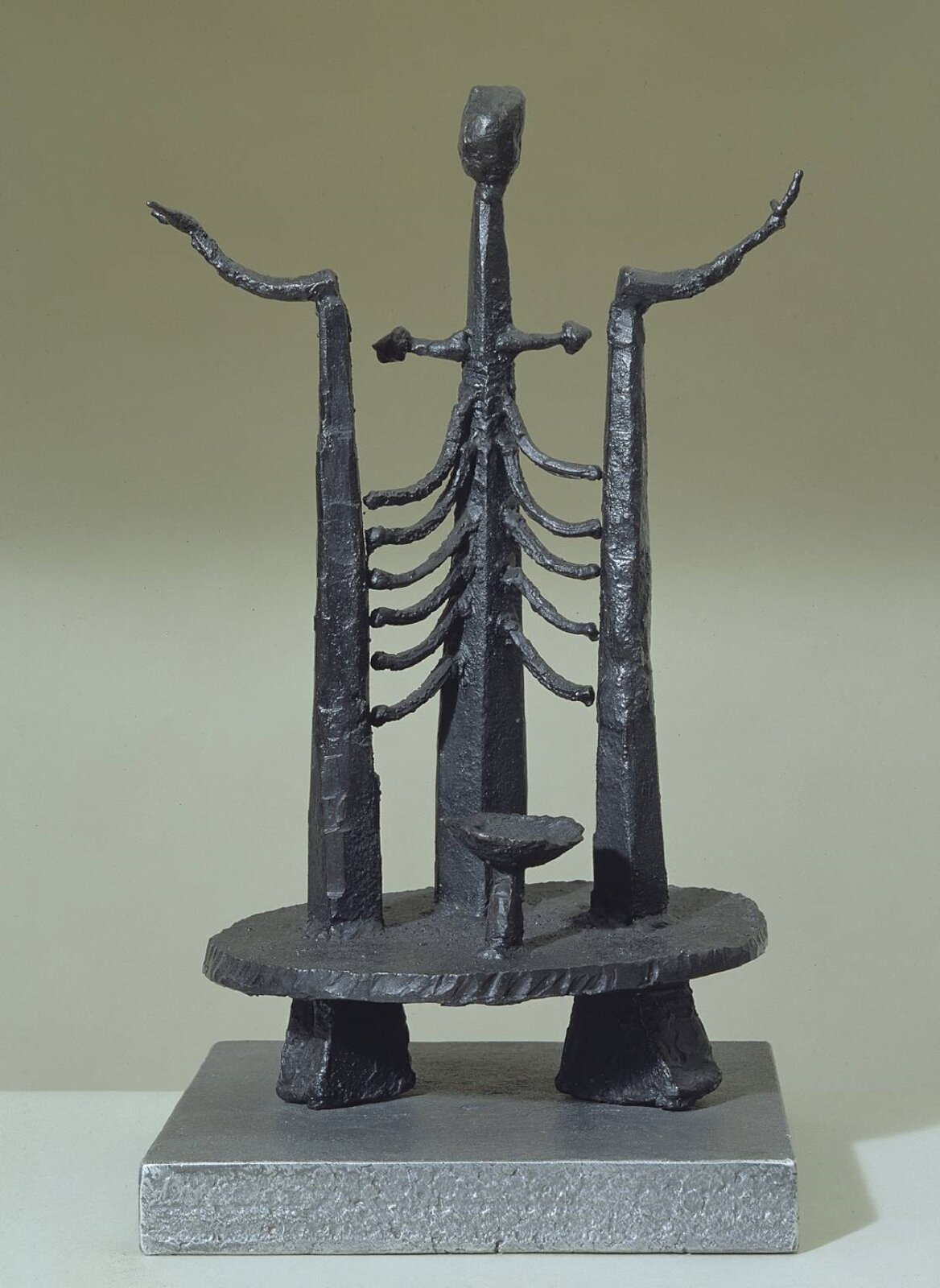 Geoffrey Clarke, „Kobieta” Umieszczona na niewielkim podwyższeniu rzeźba składa się z kilku elementów. Jej podstawę stanowią trzy pionowe elementy, których górne części są zakrzywione do zewnątrz. U dołu podstawy umieszczono w pozycji horyzontalnej okrąg, na którym postawiono pionowy element łączący się z dwoma zewnętrznymi za pomocą cienkich elementów przypominających ludzkie żebra. Na górze znajduje się jest owalny fragment przypominający głowę. Rzeźba jest ciemna, jednolita. Tło stanowi jasna ściana.