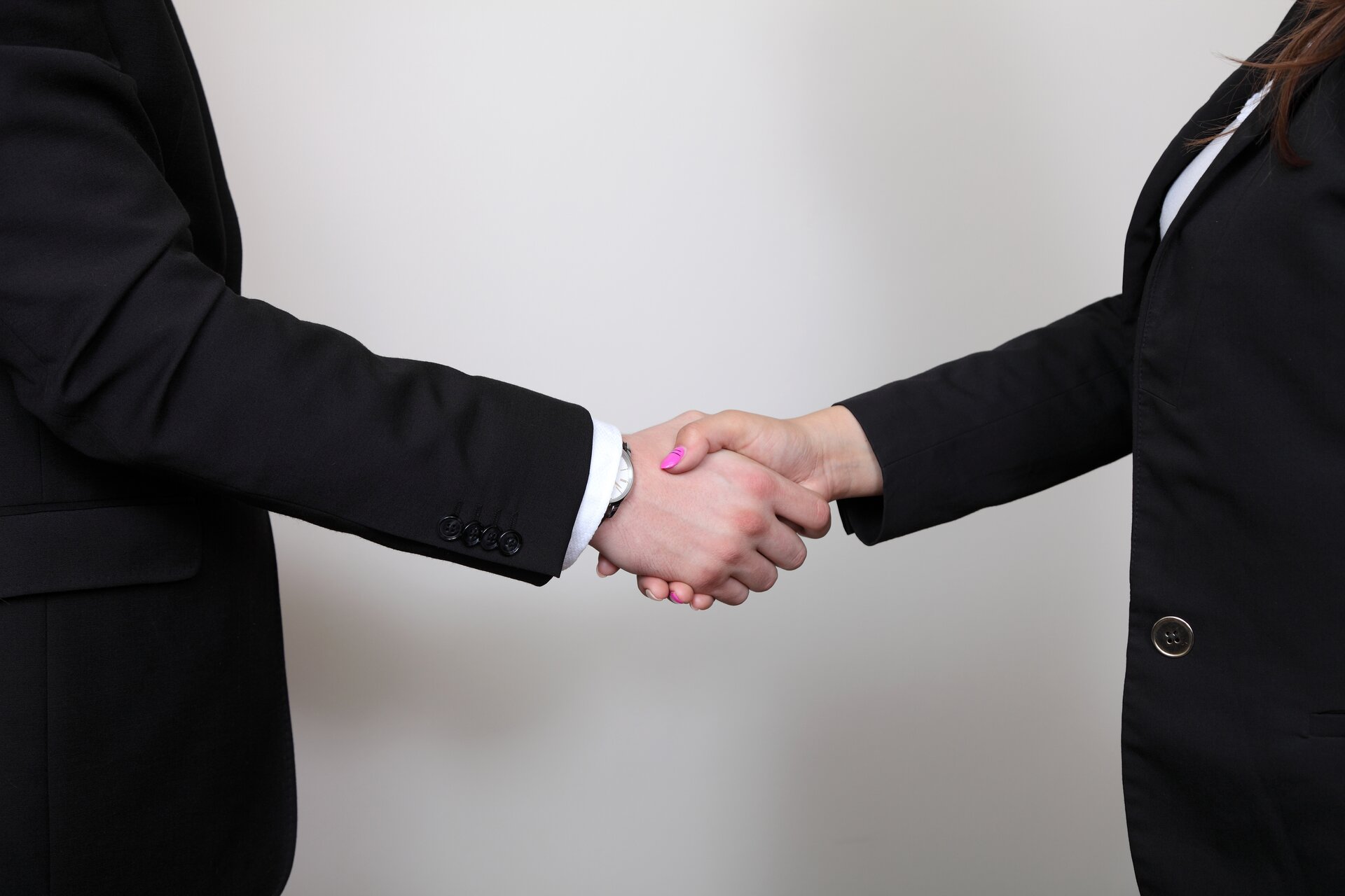 Ilustracja przedstawia dwie osoby podające sobie ręce. Osoby ubrane są w garnitury. W tle znajduje się szara ściana.