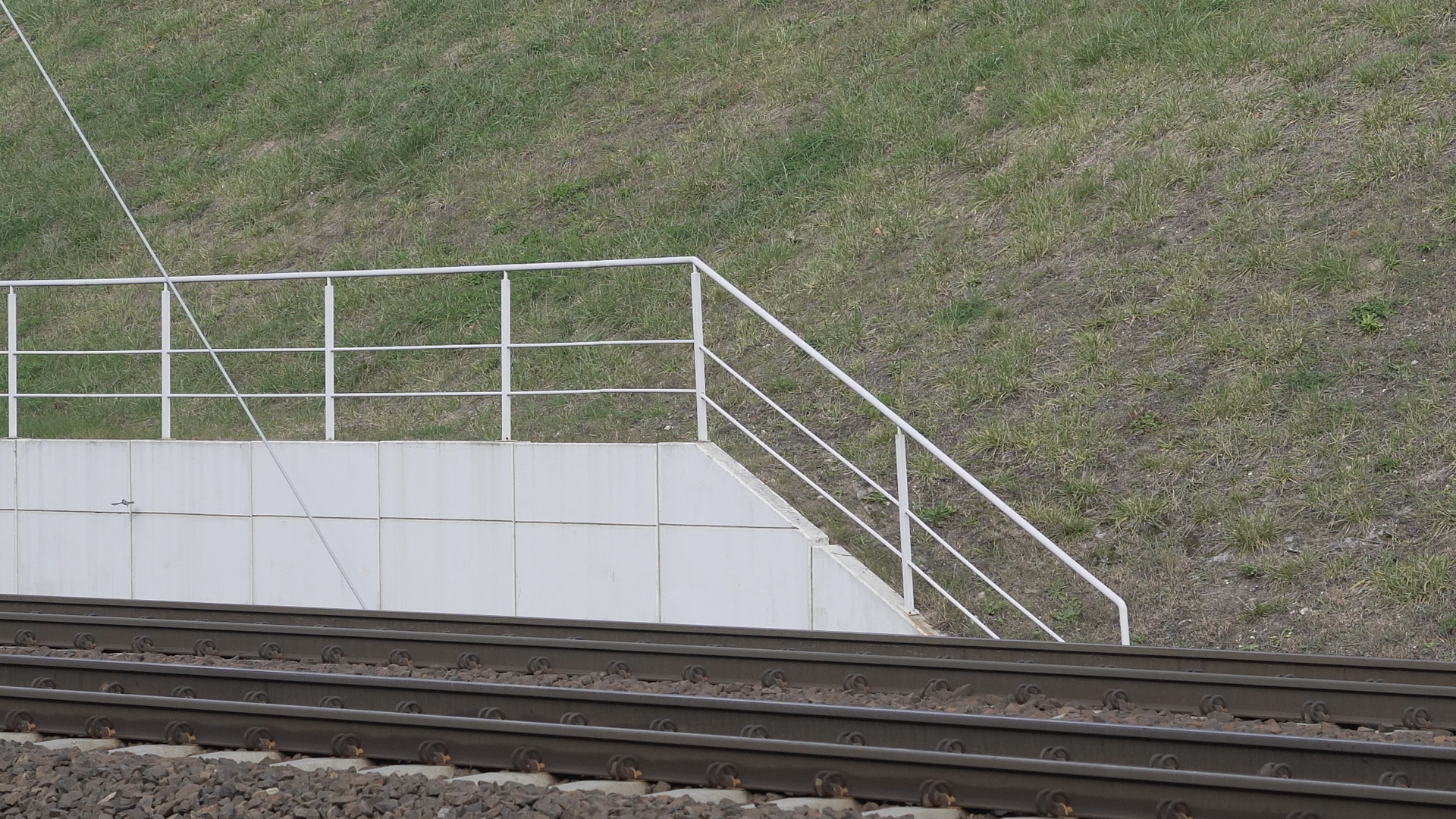  Zdjęcie przedstawia nowoczesny mur oporowy znajdujący się przed tunelem kolejowym. Mur został wykonany z prefabrykowanych, połączonych ze sobą płyt. Na szczycie muru umieszczona jest balustrada.