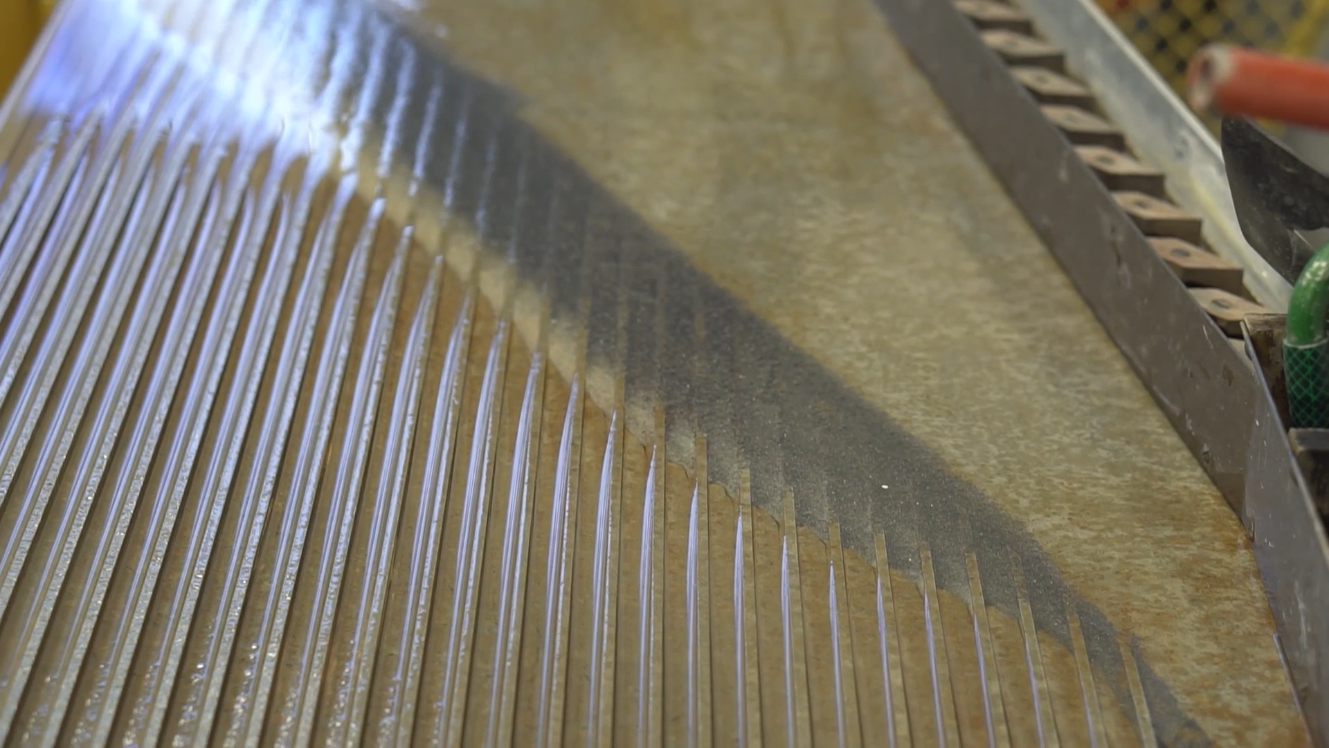 Zdjęcie przedstawia wierzchnią część stołu koncentracyjnego. Jest ona rowkowana od górnej do dolnej części, z której spływa cieczy wraz z zawieszoną w niej nadawą, Powierzchnia stołu jest nachylona pod pewnym kątem do płaszczyzny poziomej celem umożliwienia swobodnego przepływu i rozdziału nadawy. Na stole znajdują się ziarna rozmieszczone pasmami od lewego górnego rogu stołu do prawego dolnego, czyli po przekątnej. Po prawej stronie znajdują się jasne drobiny. Na środku ciemnoszare. A w okolicach przekątnej stołu najjaśniejsze. Poniżej zdjęcia znajduje się przycisk multimedialny z nagraniem audio. Treść nagrania jest zgodna z tytułem zdjęcia.