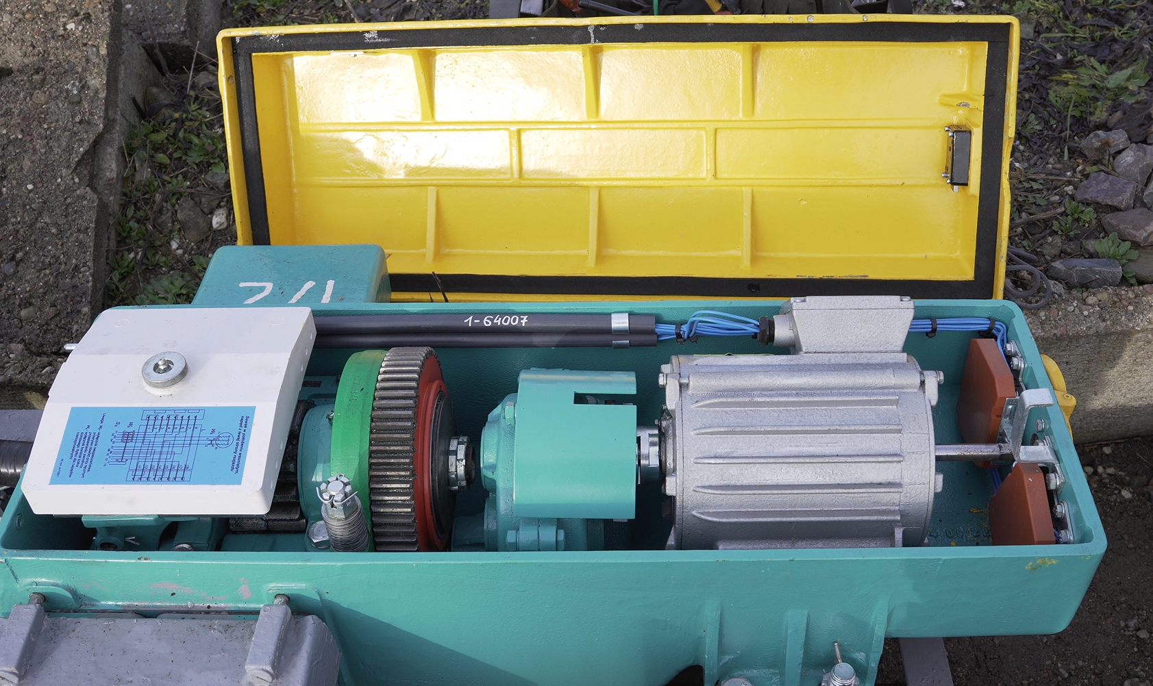 Zdjęcie przedstawia Napęd zwrotnicowy. Widoczna jest skrzynka z napędem. Jej wieko jest zdjęte i leży obok skrzynki. Wewnątrz widoczne są cylindryczne motory oraz kable.