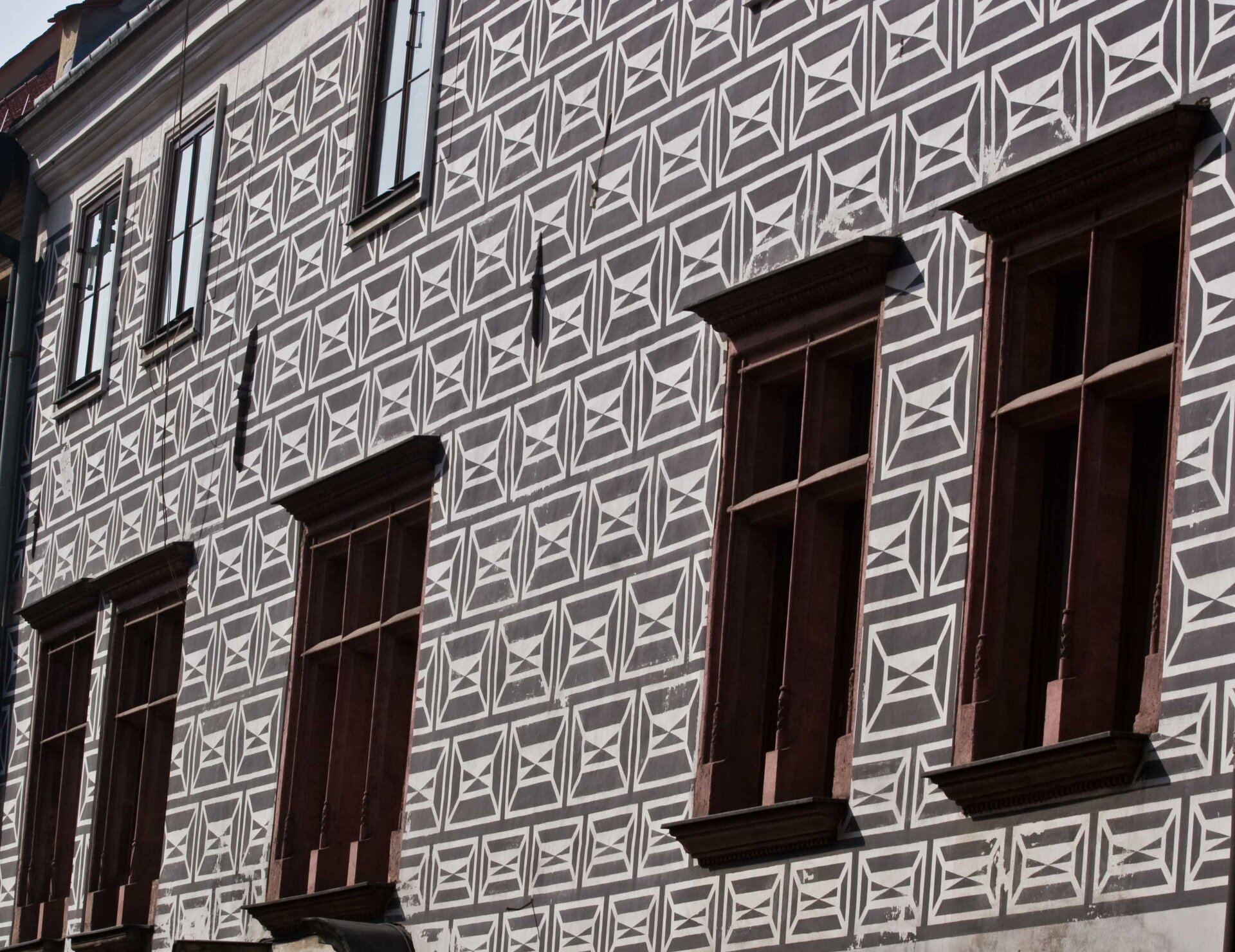 Ilustracja przedstawia sgraffito wykonane na fasadzie budynku. Dekoracja imituje renesansowe okładziny kamienne w kolorze jasnoszarym na ciemnoszarym tle.
