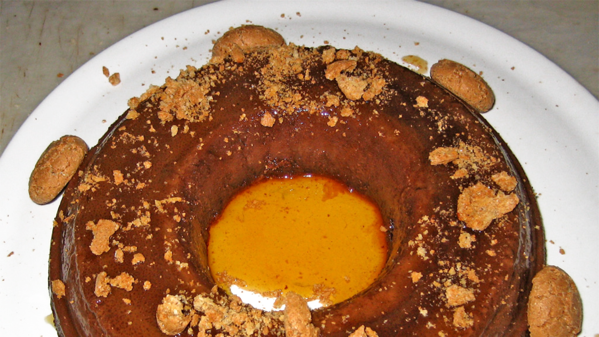 Zdjęcie przedstawia deser Bonèt. Deser to okrągły pudding z dodatkiem kakao. Wokół deseru leżą migdały.