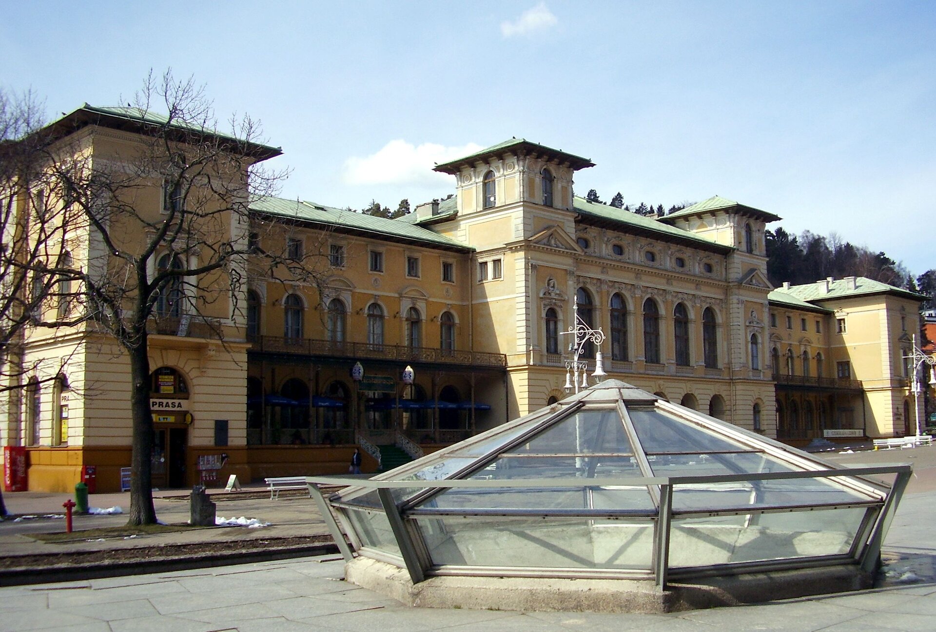 Na zdjęciu budynek pijalni wód z końca dziewiętnastego wieku. Wykonany w stylu neorenesansowym. Liczne okna zakończone łukami z ozdobnikami, ściany koloru piaskowego, rozległa, podłużna bryła budynku przypominająca architekturę pałacową.