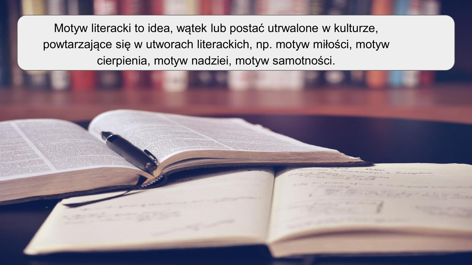 Zdjęcie przedstawia dwie otwarte książki leżące na ciemnym blacie. Bliżej obiektywu znajduje się otwarty zeszyt z zapisami, które są nieczytelne. Na jego lewym górnym rogu leży otwarta książka, na której leży czarne pióro. W tle widoczne są kolorowe grzbiety książek. U góry zdjęcia znajduje się napis: „Motyw literacki to idea, wątek lub postać utrwalone w kulturze, powtarzające się w utworach literackich, np. motyw miłości, motyw cierpienia, motyw idei, motyw samotności”. 