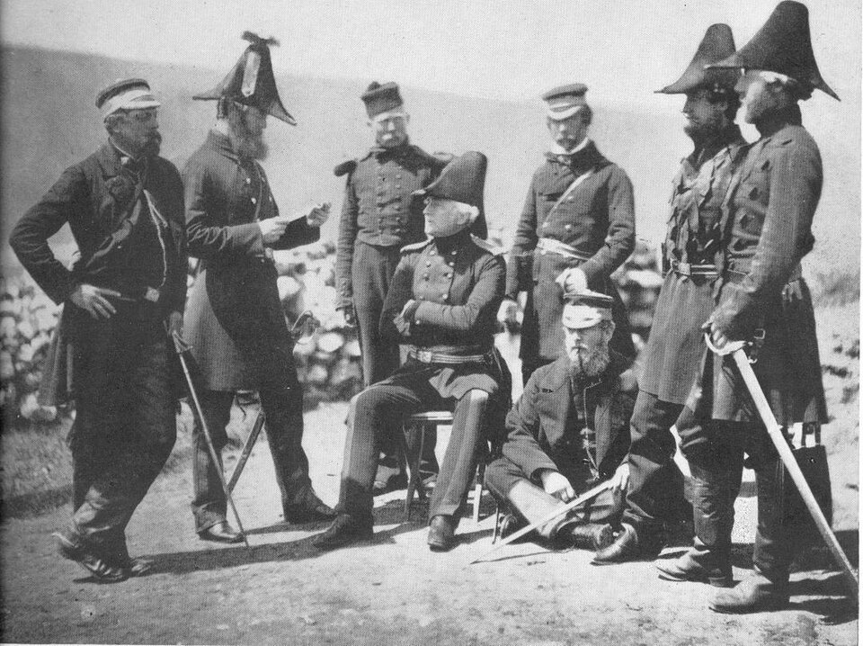 Czarno‑biała fotografia przedstawia Georga Browna siedzącego na drewnianym krzesełku. Jest on ubrany w ciemny mundur i wysoką ciemną czapkę. Jest otoczony przez umundurowanych oficerów. Jeden z nich czyta coś z kartki, a Brown go słucha. Panowie znajdują się na otwartej przestrzeni. 