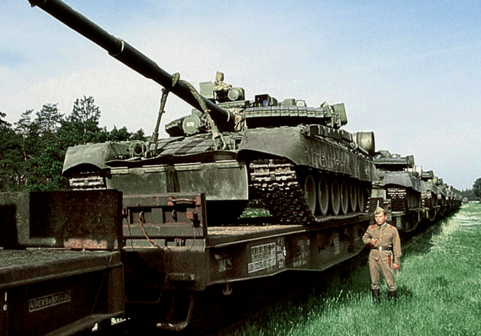 Zdjęcie przedstawia pociąg wiozący na platformach radzieckie czołgi. Przy torach stoi radziecki żołnierz z bronią na ramieniu.