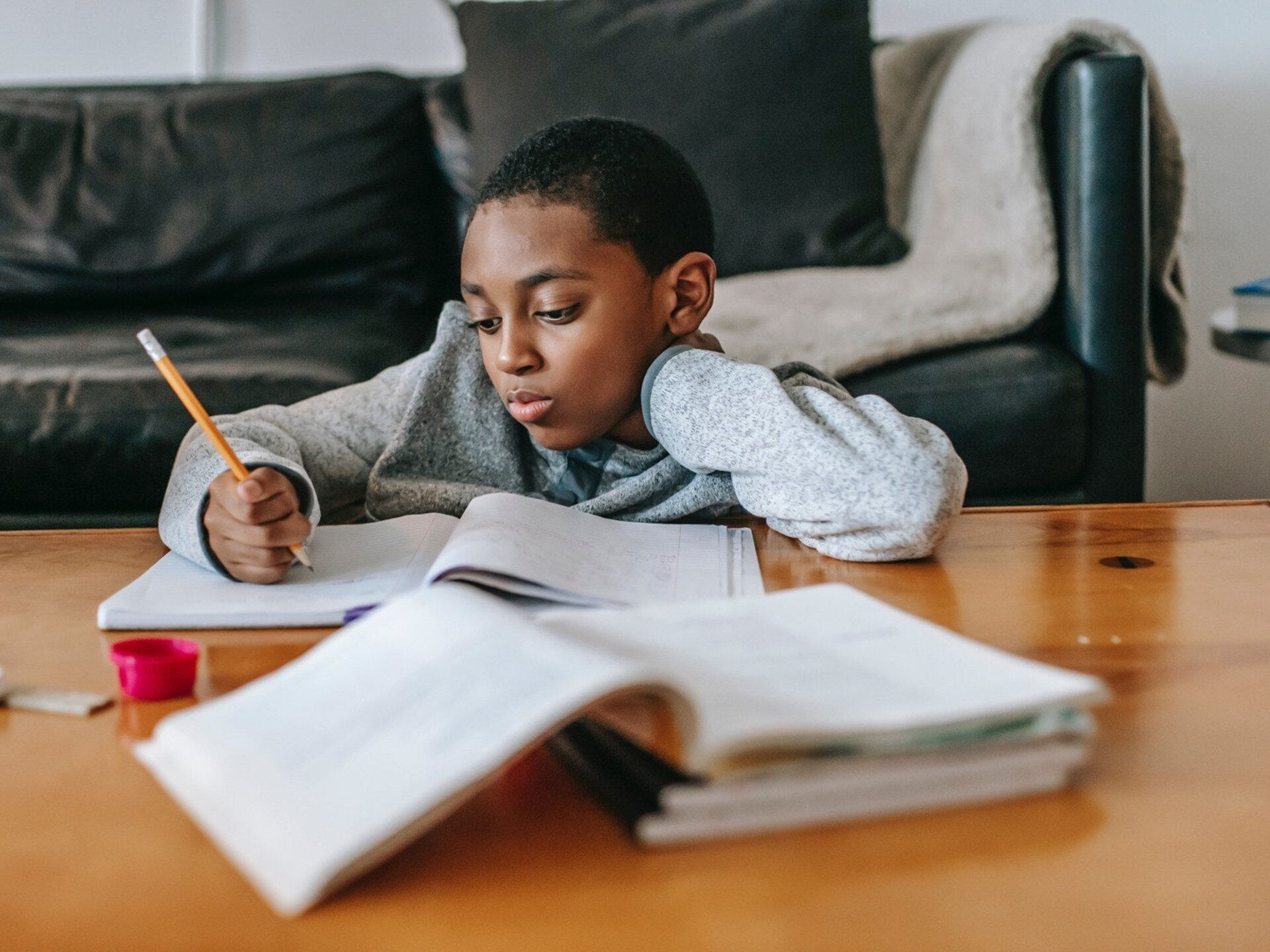 Zdjęcie przedstawia chłopca w wieku szkolnym siedzącego przy stole i piszącego coś w zeszycie.