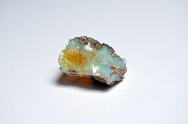 Zdjęcie przedstawia opal. Minerał ten przypomina szklistą muszlę z żółtym refleksem. Opale powstają w wyniku działalności wody w skorupie ziemskiej. Jest składnikiem wielu skał osadowych, skał magmowych, spotykany jest w osadach gejzerów i gorących źródeł.