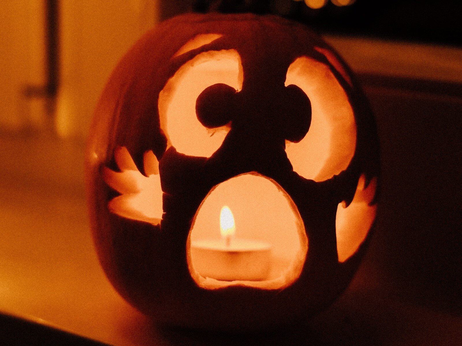 Zdjęcie przedstawia dynię z z wydrążonymi oczami i ustami, w środku której pali się świeca.  