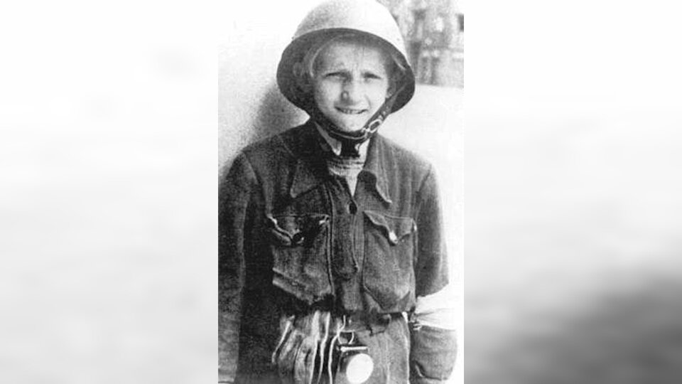 Zdjęcie przedstawia młodego powstańca. Chłopak ubrany jest w mundurek z kołnierzem. Na głowie ma wojskowy hełm.