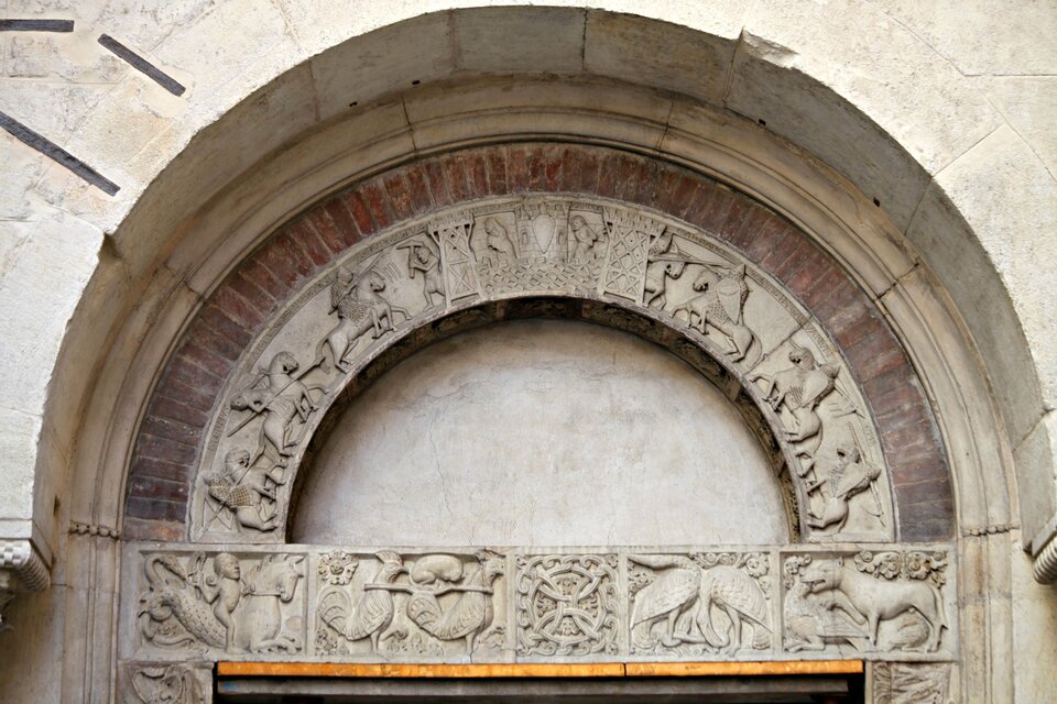 Fotografia przedstawiająca portal Pescherie. Na zdjęciu znajduje się nadproże z tympanonem i archiwoltami. Pole tympanonu jest gładkie, pozbawione dekoracji. Nadproże oraz szeroka archiwolta są wypełnione płaskorzeźbami przedstawiającymi jeźdźców, zwierzęta, dekoracje abstrakcyjne.