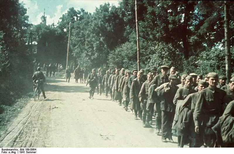 Kliknij, aby powiększyć Na zdjęciu mężczyźni ubrani w rosyjskie mundury idą prawą stroną drogi. Jest ich ponad setka. Są bez broni. Obok nich idą niemieccy żołnierze. Jest ich kilku. Jeden z nich jest na rowerze.