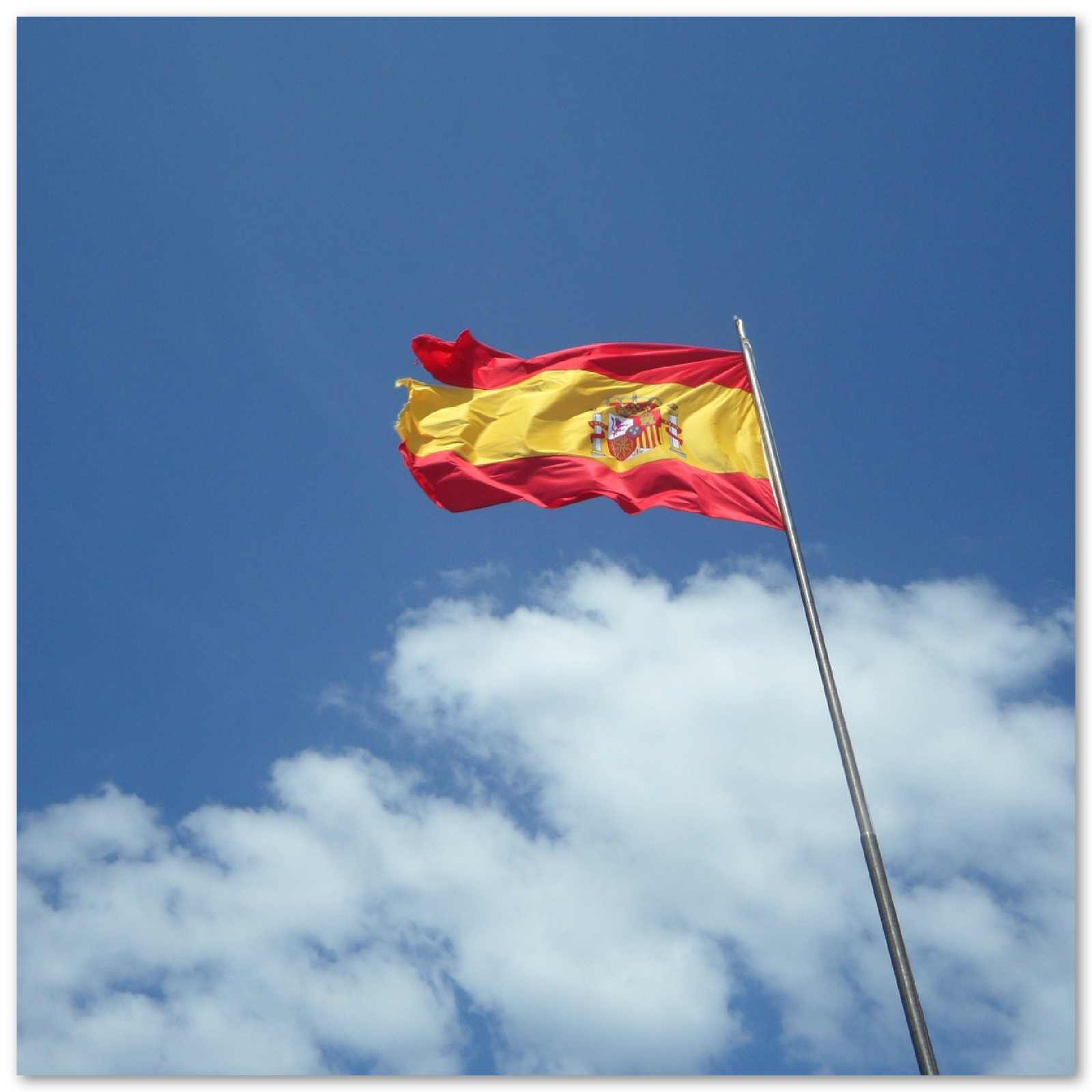 Grafika przedstawia hiszpańską flagę powiewającą na wietrze na tle nieba.
