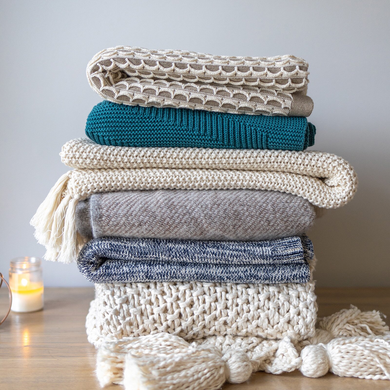 Zdjęcie przedstawia złożone koce, ułożone jeden na drugim w kolorach szarym, niebieskim i białym.