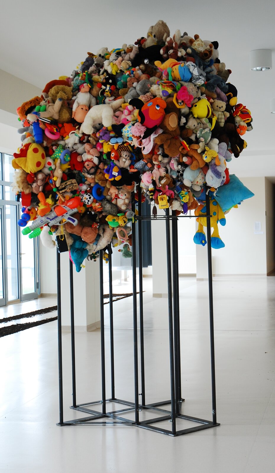 Ilustracja przedstawia dzieło Katarzyny Adaszewskiej pt. „ Enfant terrible  [czytaj: ąfą terible] II”. Praca przedstawia zabawki, ciasno jedna przy drugiej, umieszczone na metalowej konstrukcji. Wśród zabawek dominują pluszaki w różnych kolorach. Są to głównie zwierzęta, postacie z bajek i plastikowe zabawki. Sposób kompozycji przypomina koronę drzewa z pluszaków, umieszczoną na konarze z metalowych prętów.