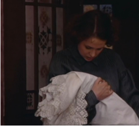 Zdjęcie przedstawia kobietę w ciemnoniebieskiej koszuli, która trzyma złożone białe materiały. Ma pochyloną głowę.