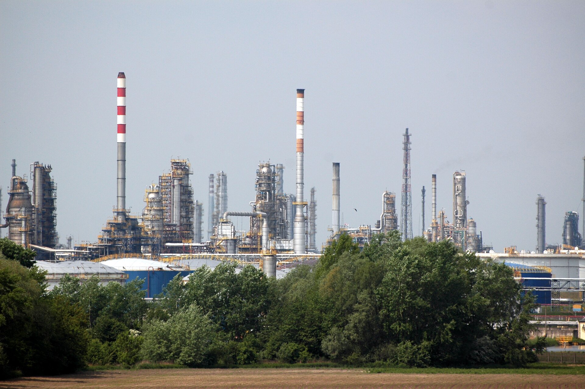 Na zdjęciu kombinat rafineryjno‑petrochemiczny PKN ORLEN w Płocku. Budynki otoczone są wysokimi, wąskimi kominami.