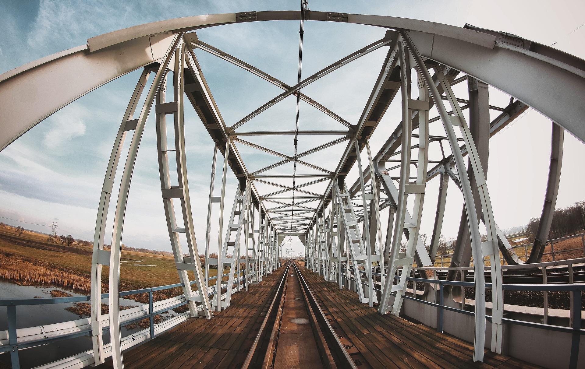 Zdjęcie przedstawia stalowy most. Wiodą przez niego tory kolejowe.