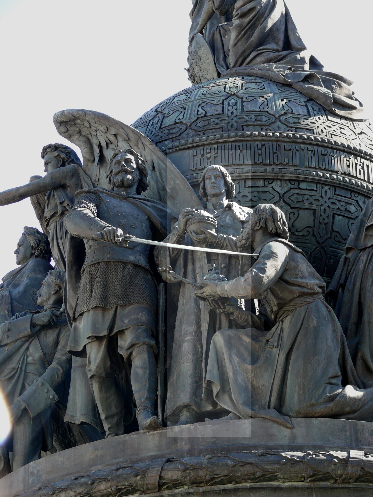 Zdjęcie przedstawia fragment pomnika. Widać na nim kilka postaci. Mężczyzna w stroju rycerza z wąsem i brodą trzyma w prawej dłoni szablę i kieruje jej ostrze w stronę klęczącego starszego mężczyzny w szatach. Za nimi stoi młody chłopak trzymający w dłoniach jabłko królewskie. Z tyłu widać postać anioła ze skrzydłami oraz inne postaci.