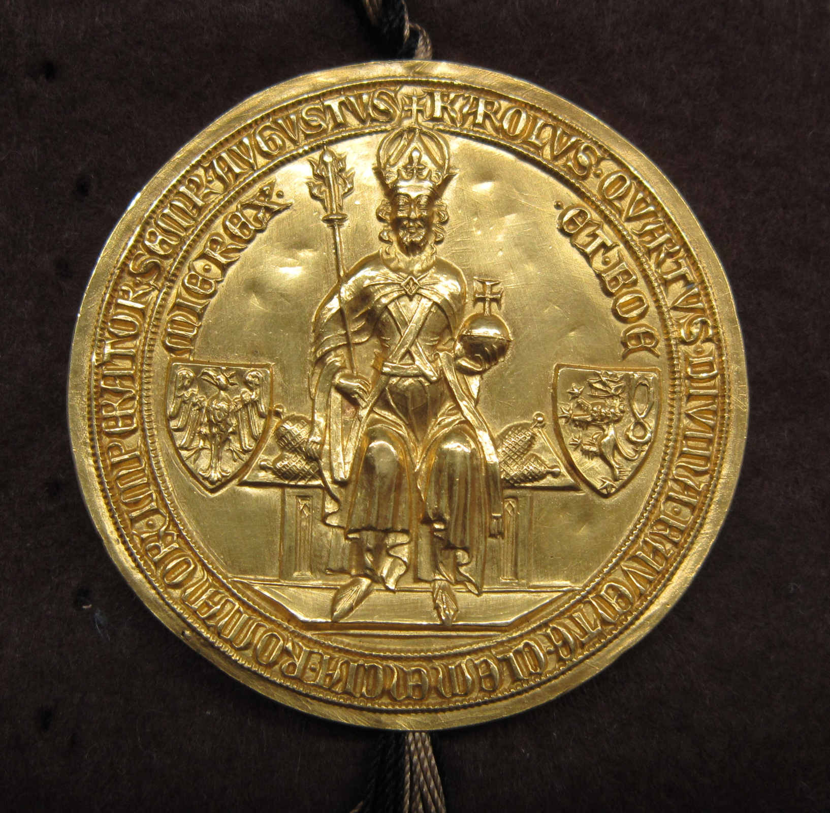 Na zdjęciu znajduje się okrągła, złota pieczęć z cesarzem Karolem czwartym Luksemburskim. Siedzi on na tronie w koronie i trzyma w rękach królewskie jabłko i berło. Po obu jego stronach znajdują się herby. Na brzegach pieczęci znajdują się liczne napisy. 